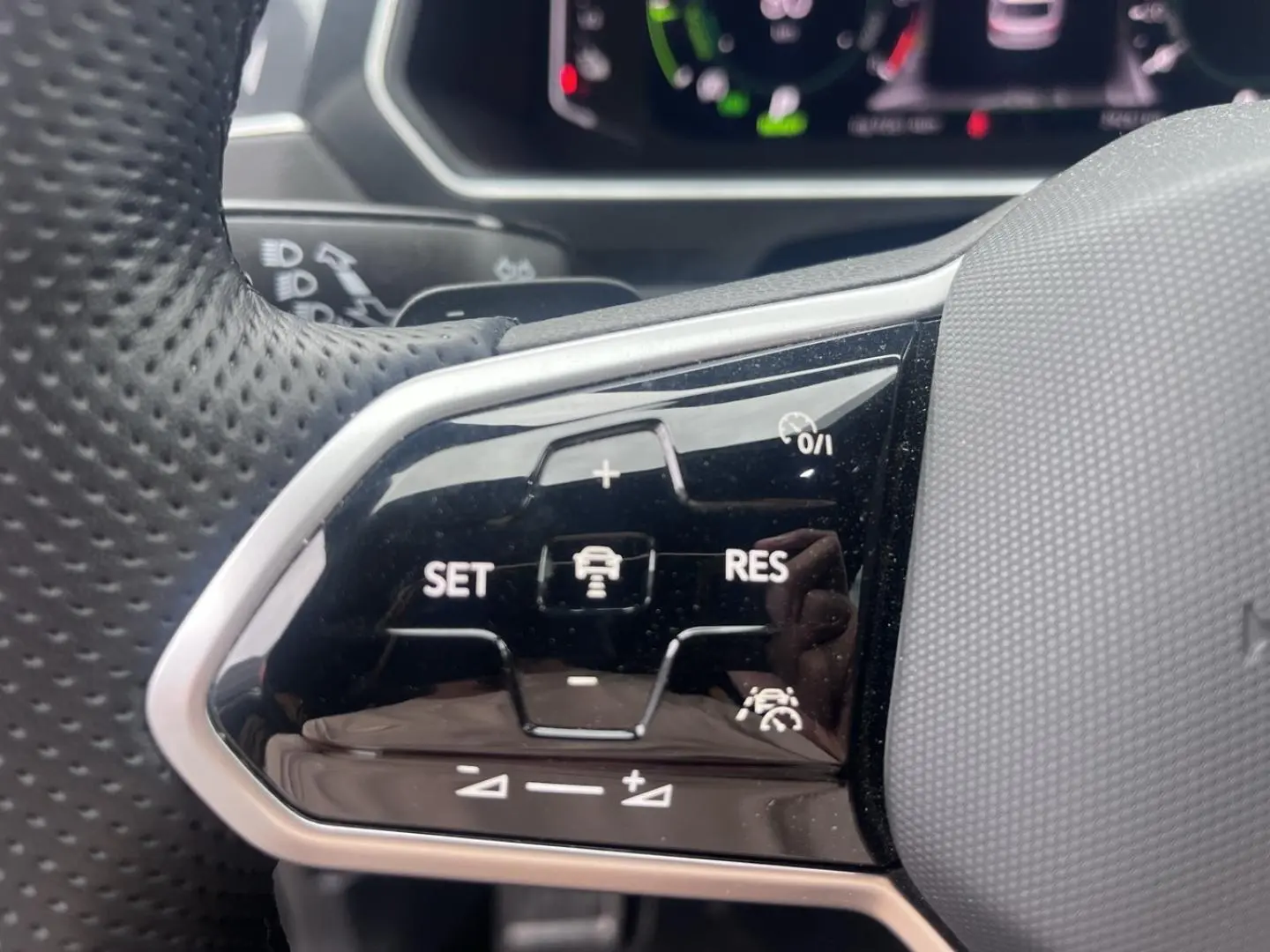 Gros plan sur les commandes de régulateur adaptatif du volant cuir perforé du Volkswagen Tiguan gris Dauphin 2023.