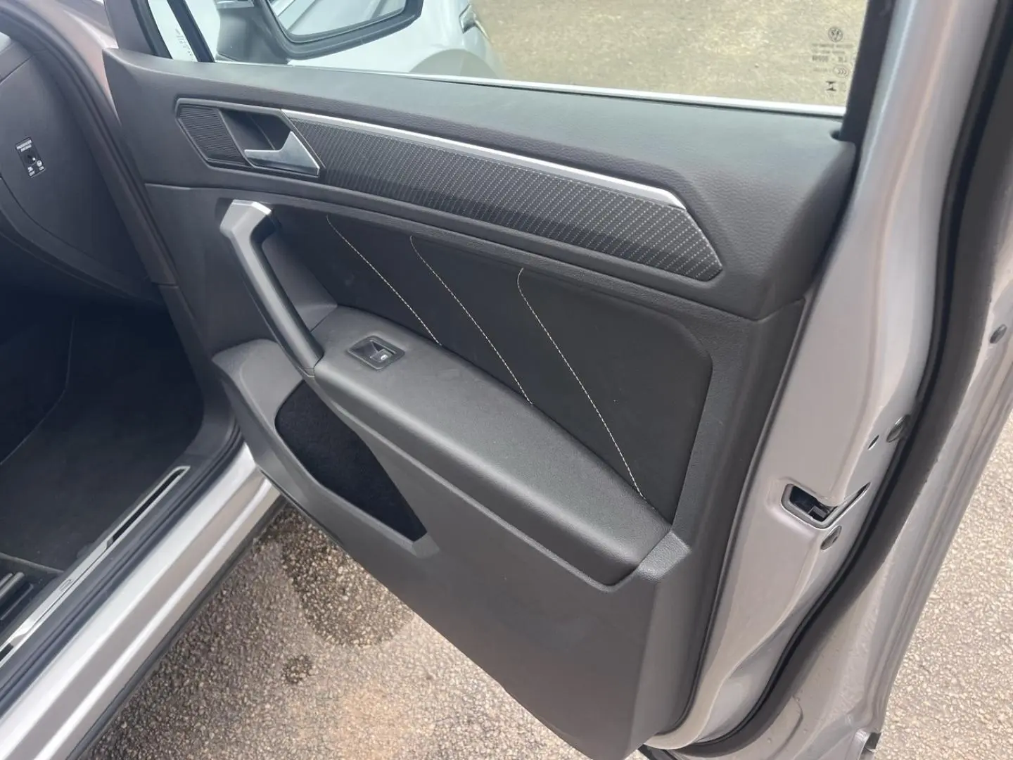 Vue intérieure de la porte avant gauche du Volkswagen Tiguan gris dauphin avec insert carbone et surpiqûres blanches.