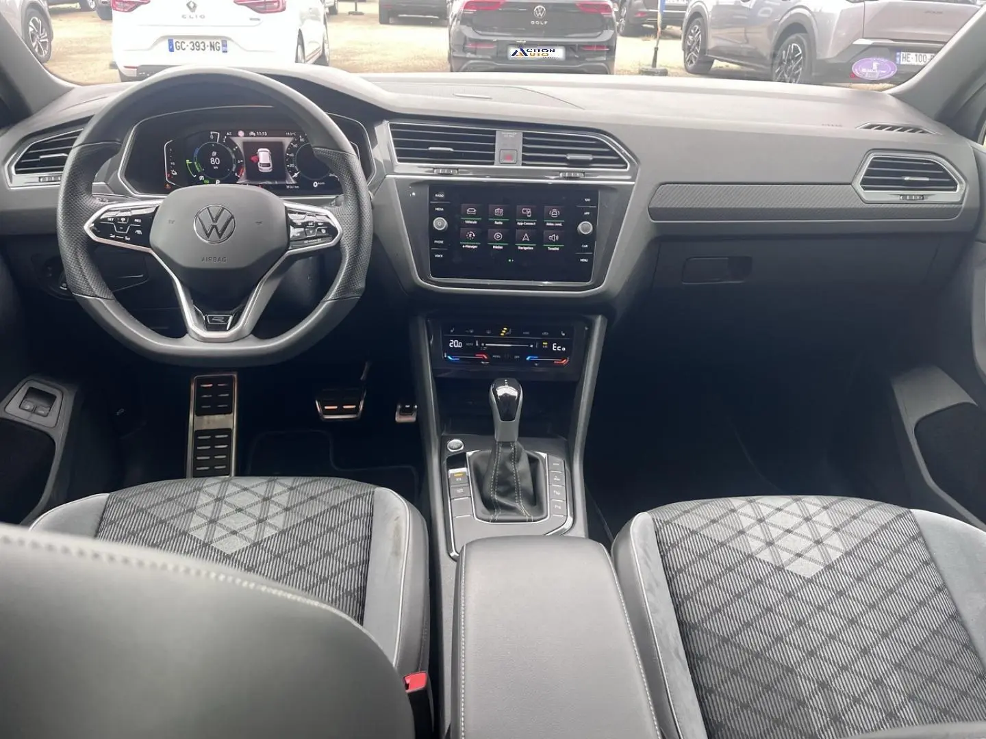 Vue intérieure avant du Volkswagen Tiguan 1.4 eHybrid gris, montrant volant multifonction, écran tactile et sièges sport à motifs.