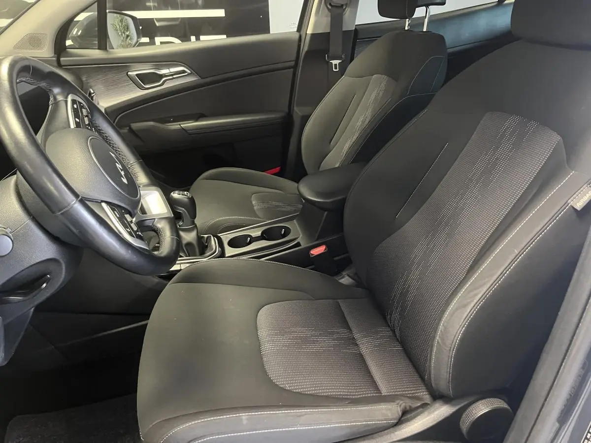 Intérieur avant du Kia Sportage 2022, sièges tissu noir, volant cuir et console centrale avec boîte manuelle.
