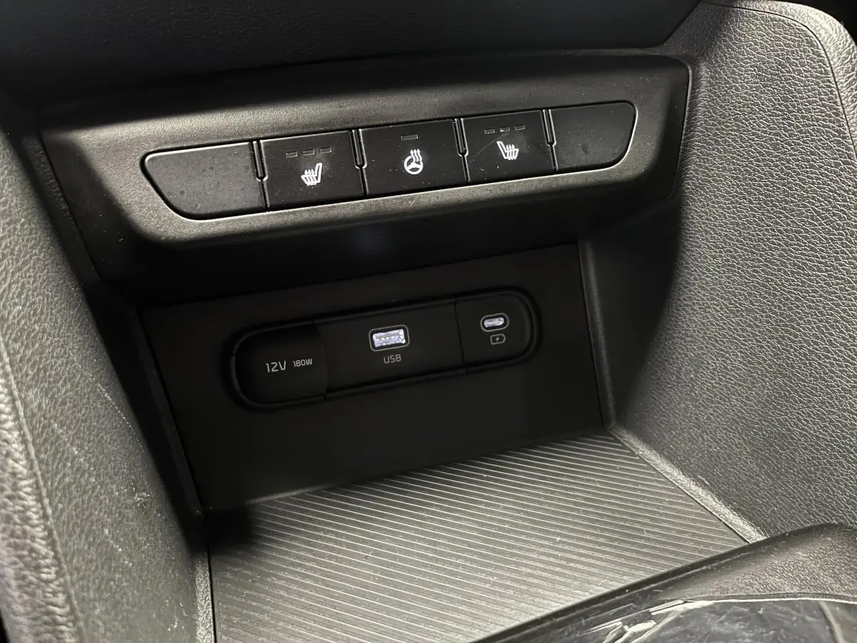 Gros plan sur la console centrale du Kia Sportage gris 2022 avec ports USB, prise 12V et commandes de sièges chauffants.