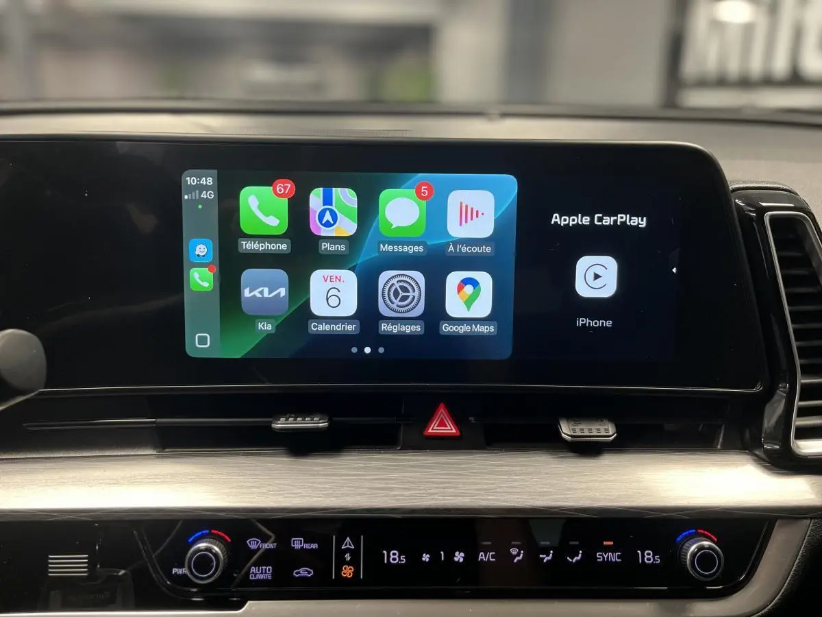 Écran tactile central affichant Apple CarPlay dans l'habitacle du Kia Sportage gris, vue rapprochée du tableau de bord.