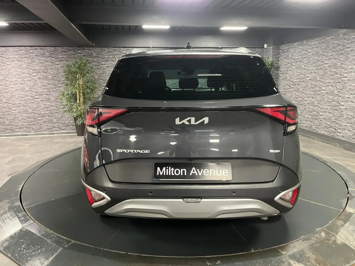 Vue arrière d'un KIA Sportage gris métallisé 2022 avec feux arrière LED et bouclier noir laqué en intérieur showroom.