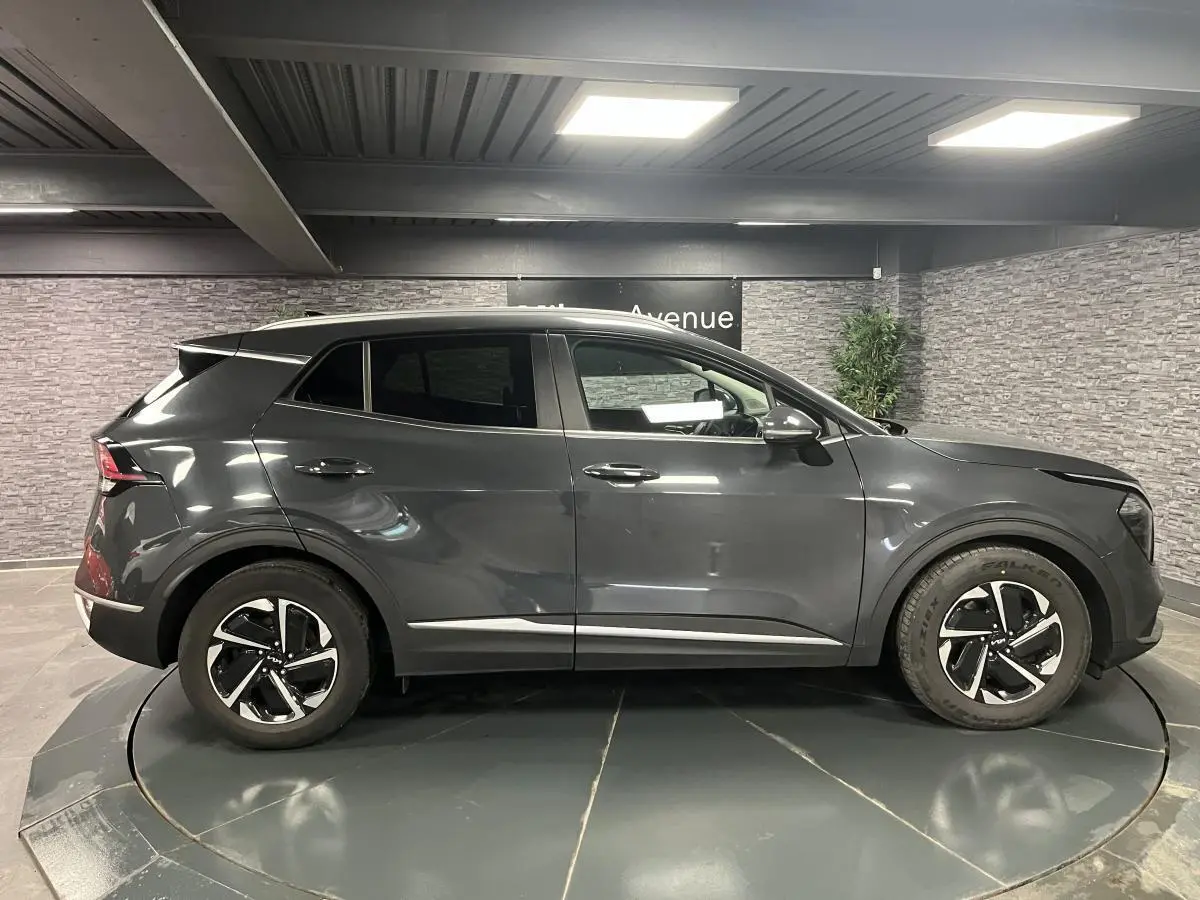 Profil côté droit du KIA SPORTAGE gris métallisé 2022 avec jantes alliage et lignes épurées en intérieur showroom.