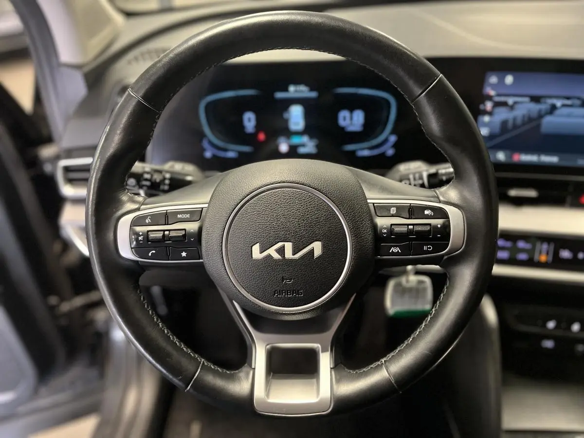 Volant cuir noir avec commandes intégrées et logo KIA, tableau de bord numérique flou en arrière-plan du Kia Sportage 2022.