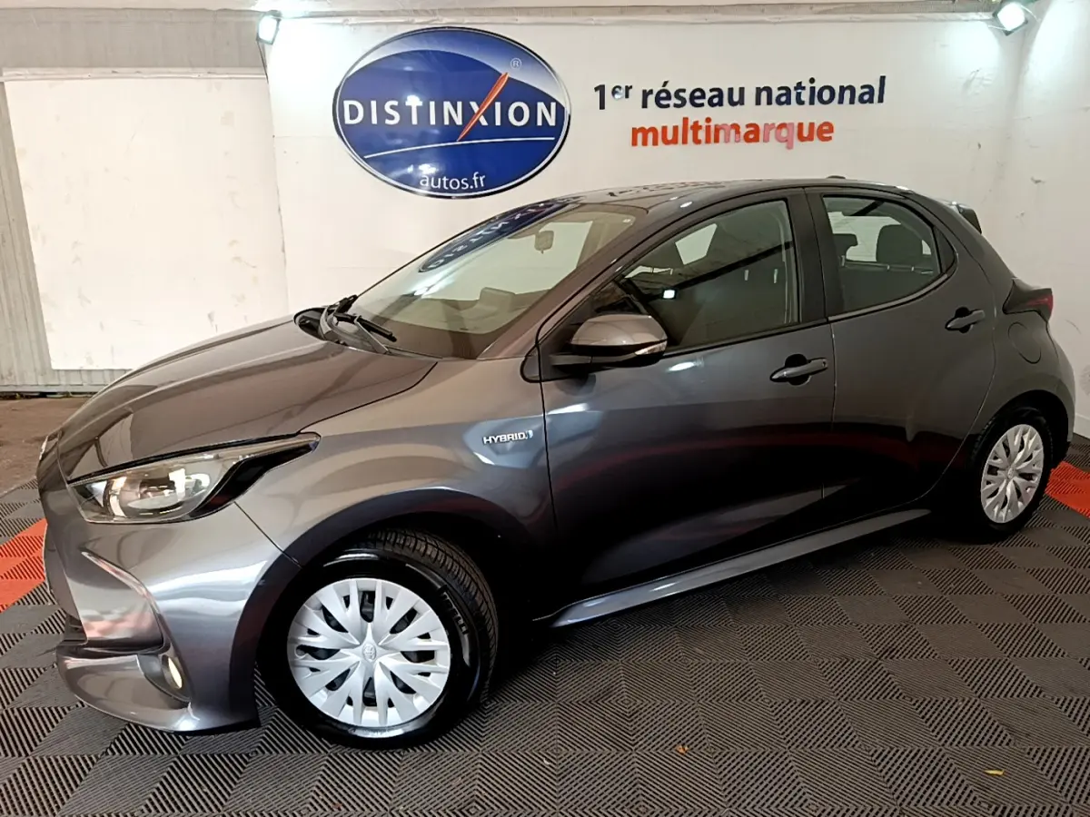Toyota Yaris hybride gris clair vue de profil côté gauche, avec logo Hybrid et feux avant allumés.