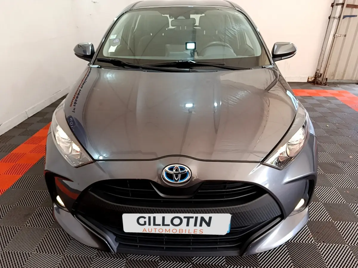 Vue frontale d'une Toyota Yaris hybride gris clair avec calandre noire et feux allumés en intérieur.