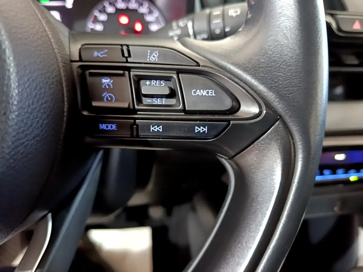 Gros plan sur les commandes du volant côté droit d'une Toyota Yaris hybride 2021, avec affichage numérique en arrière-plan.