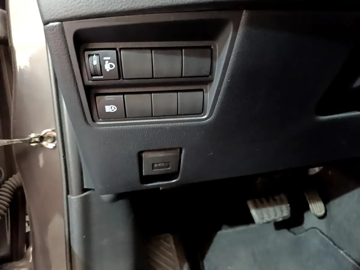 Vue rapprochée du tableau de bord côté conducteur d'une Toyota Yaris hybride gris clair, avec commandes d'éclairage et port USB visible.