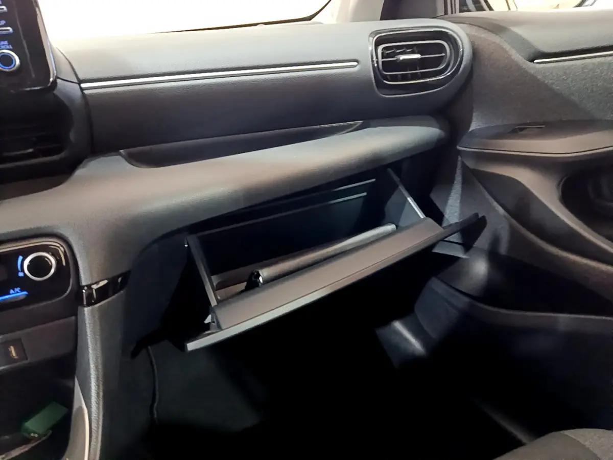 Intérieur de la Toyota Yaris Hybride 2021, vue côté passager sur la boîte à gants ouverte et tableau de bord noir.