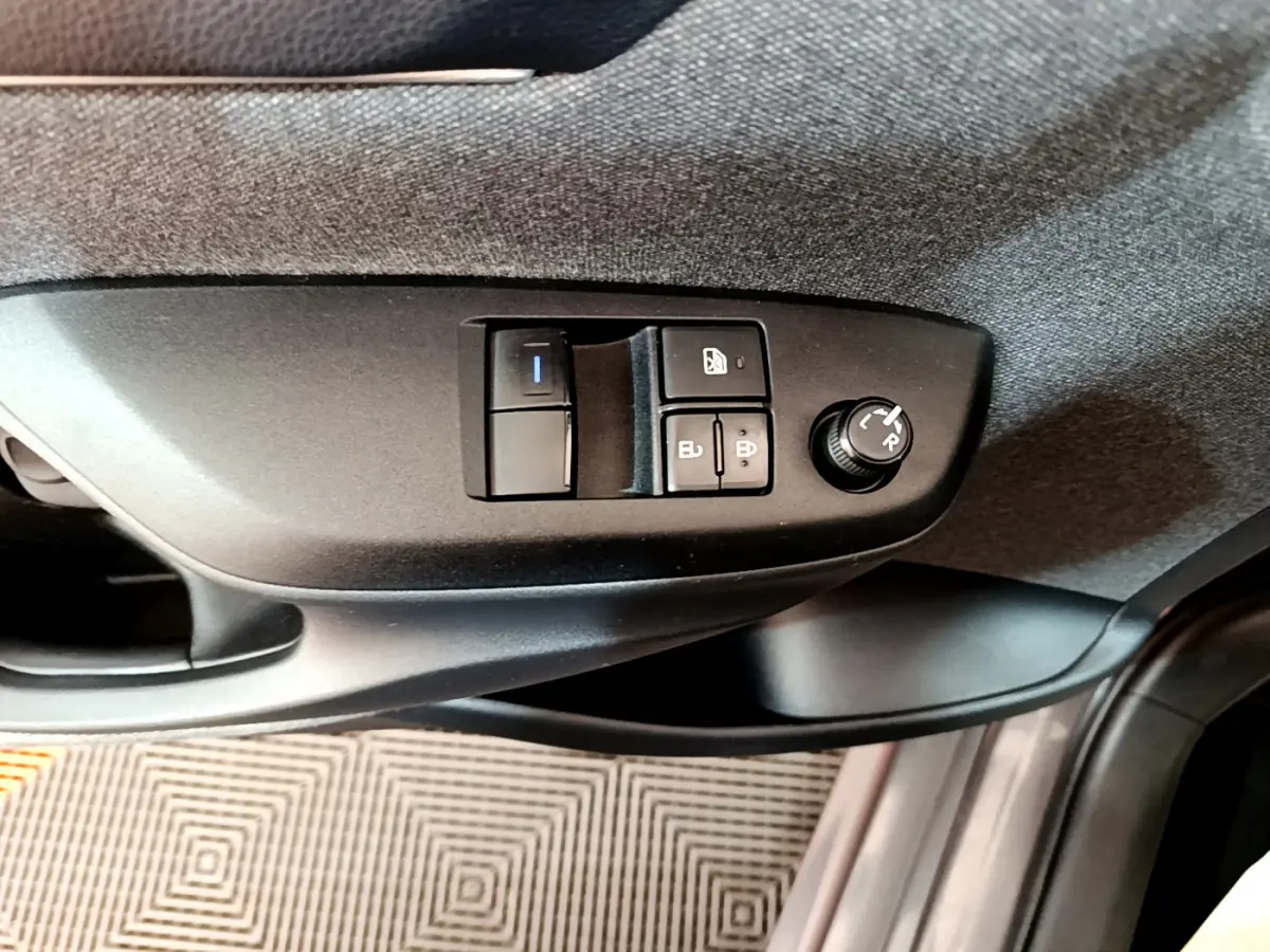 Gros plan sur les commandes de réglage des rétroviseurs et vitres côté conducteur de la Toyota Yaris hybride gris clair 2021.