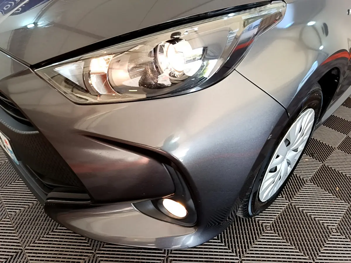 Gros plan sur l'avant droit gris clair d'une Toyota Yaris hybride 2021 avec phares et antibrouillards allumés.