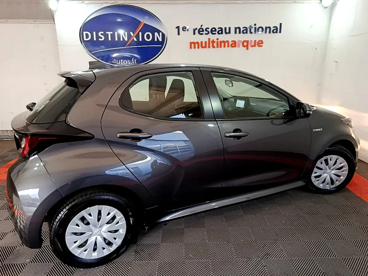 Profil droit d'une Toyota Yaris hybride gris clair 2021, avec jantes argentées et badge Hybride visible sur l'aile avant.