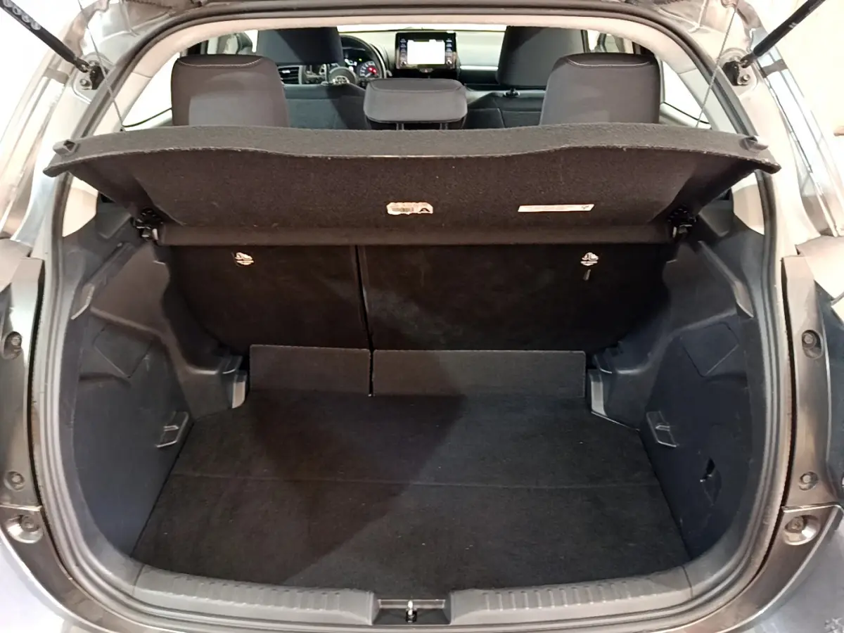 Coffre ouvert d'une Toyota Yaris hybride gris clair, vue arrière montrant l'espace de chargement et banquette arrière.