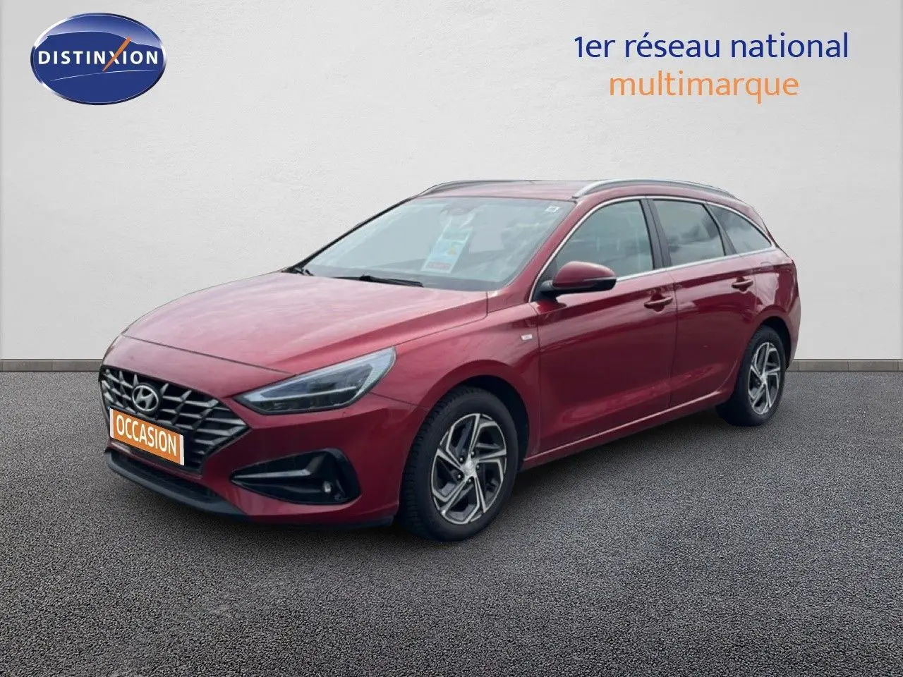 Vue 3/4 avant droite d'une Hyundai i30 SW 2023 Sunset Red Metal avec jantes alliage et calandre distinctive.