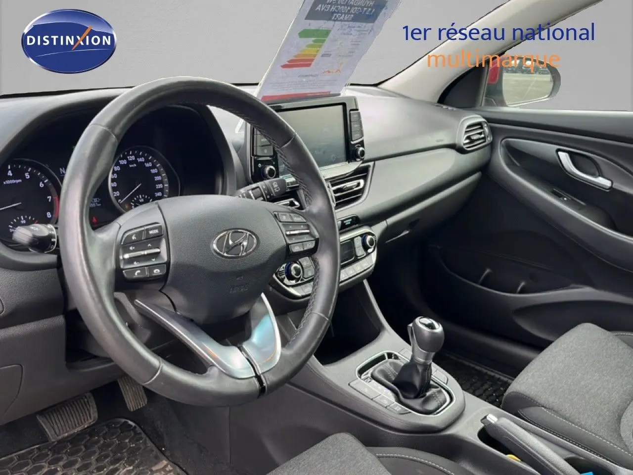 Vue intérieure côté conducteur de la Hyundai i30 SW 2023 avec tableau de bord noir et volant cuir multifonction.