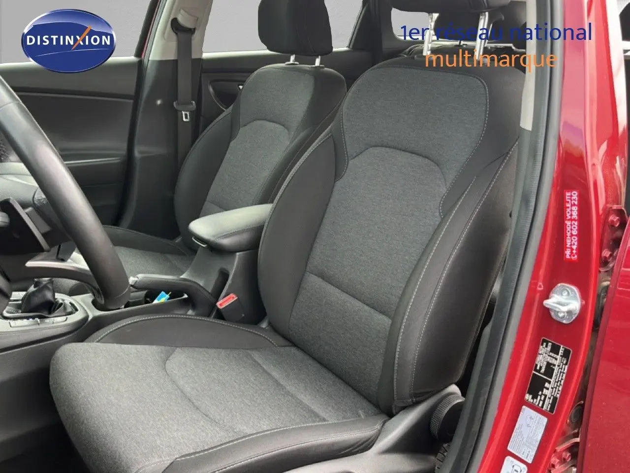Vue intérieure côté conducteur de la Hyundai i30 SW rouge, mettant en valeur les sièges tissu gris avec surpiqûres noires.