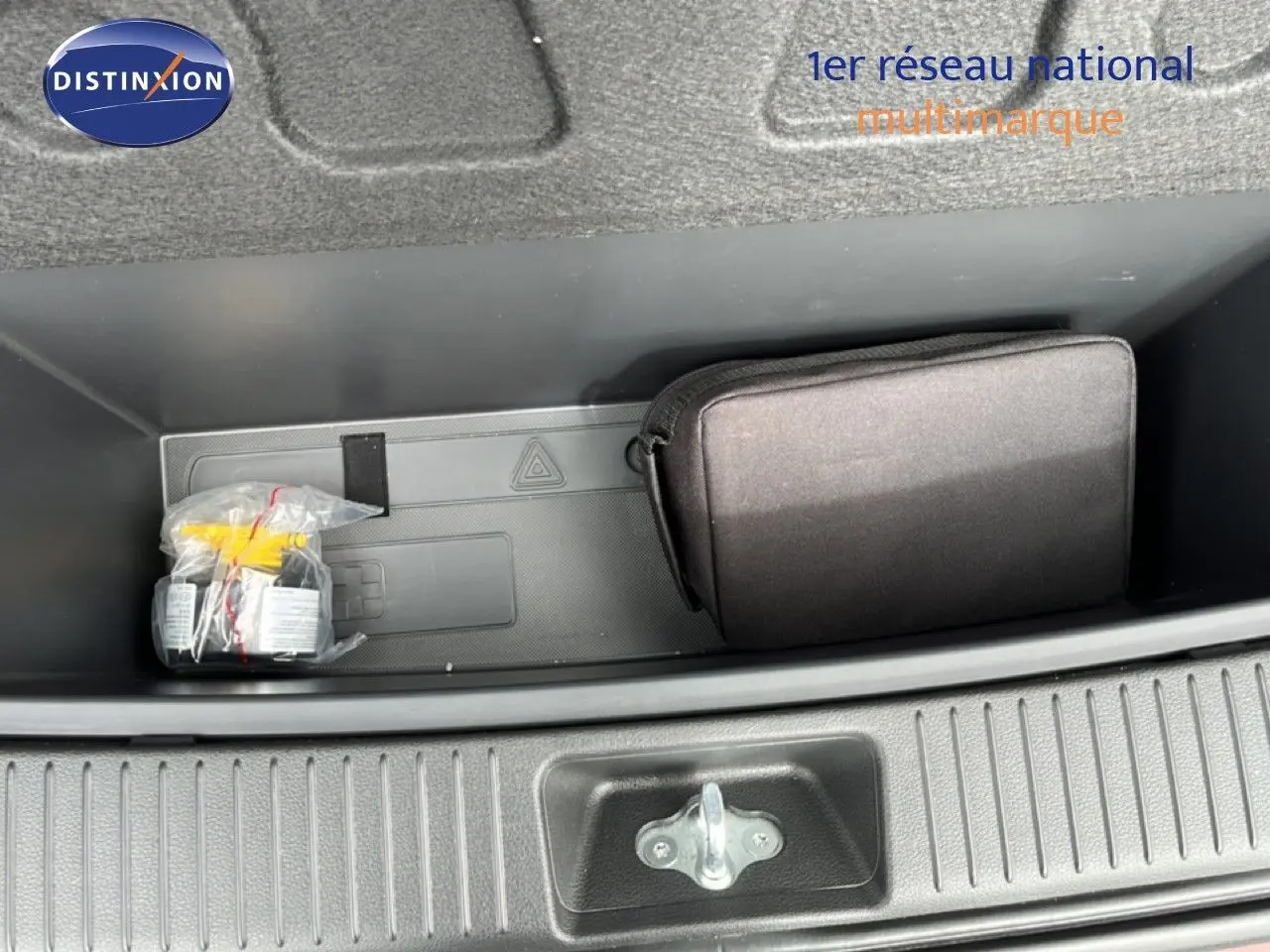 Coffre ouvert vu de dessus montrant un rangement noir avec trousse et kit de réparation sur Hyundai i30 SW rouge.