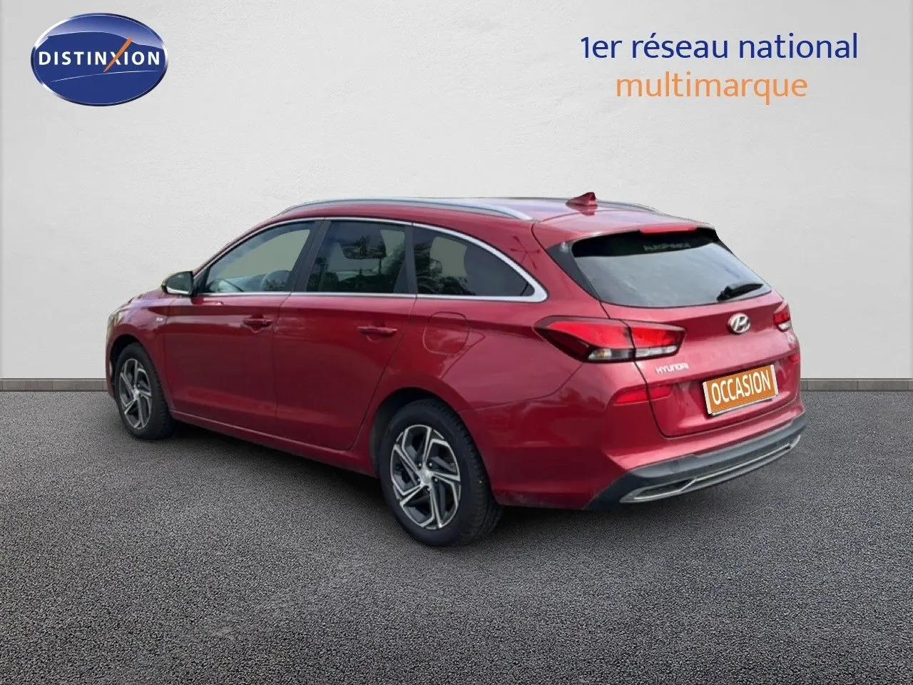 Vue 3/4 arrière droite d'une Hyundai i30 SW 2023 en rouge Sunset Red Metal avec jantes alliage bicolores.