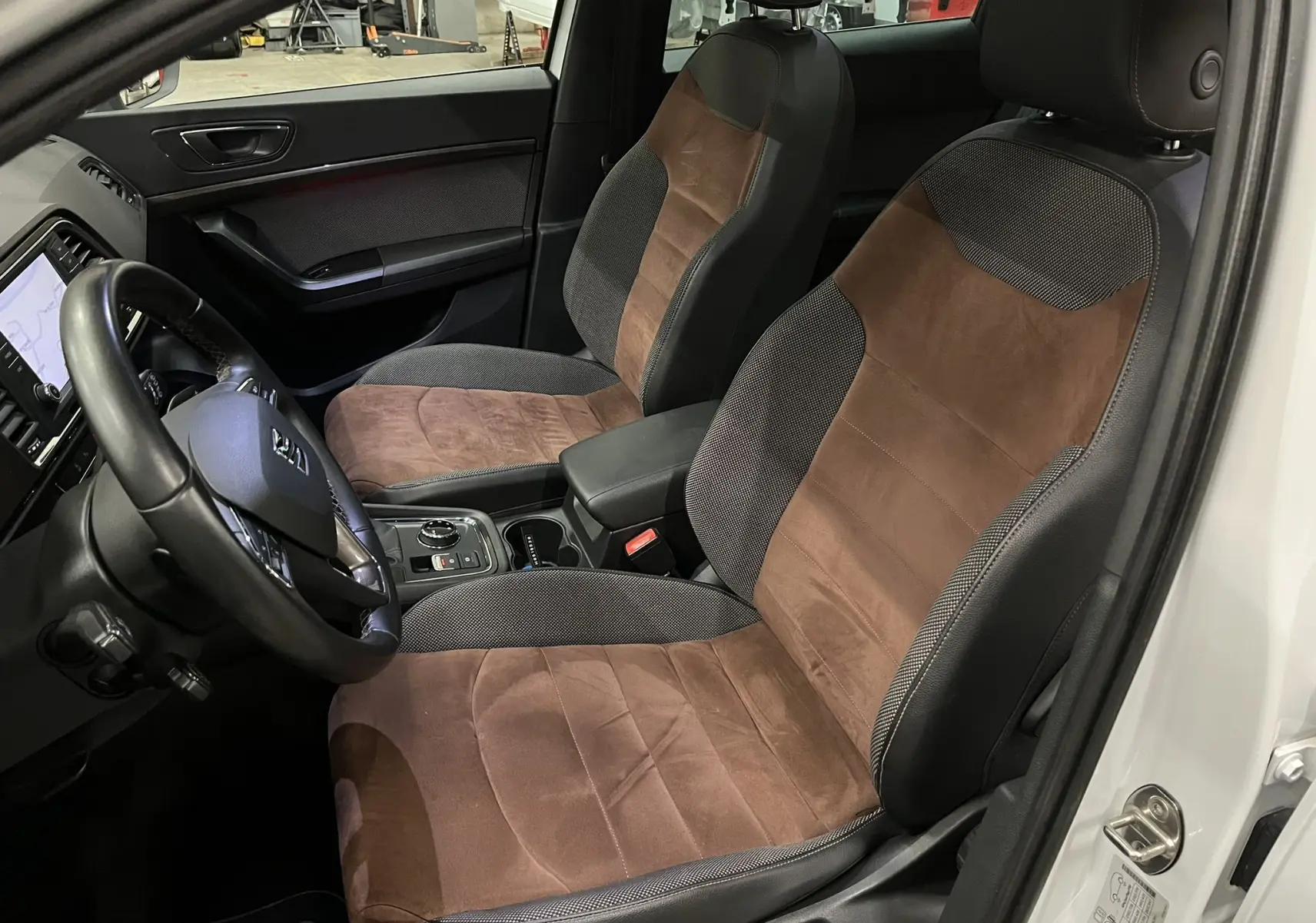 Intérieur avant du SEAT Ateca blanc, vue côté conducteur, sièges bi-matière marron et noir avec console centrale visible.