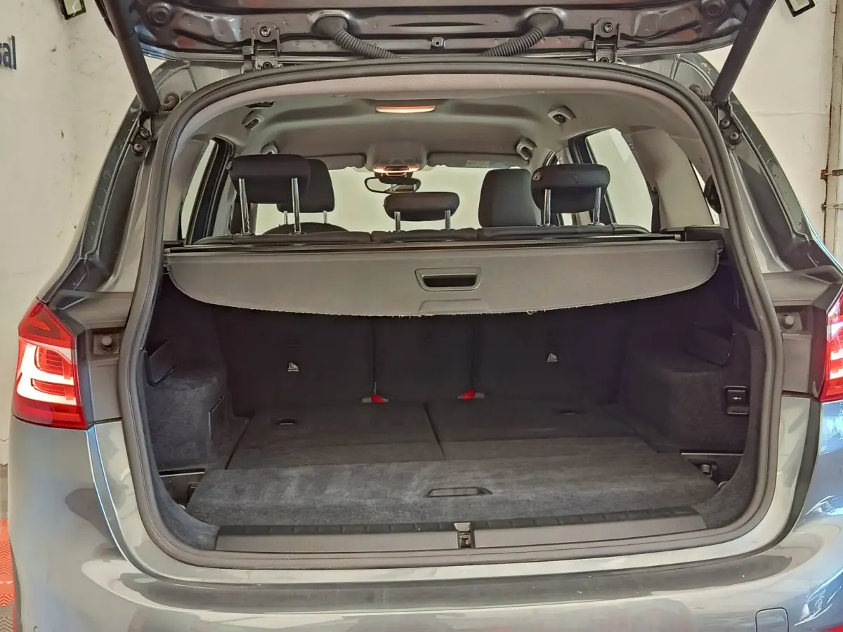 Coffre ouvert vu de l'arrière d'une BMW Série 2 Gran Tourer F46 gris clair, montrant les sièges rabattus et la tablette de coffre.
