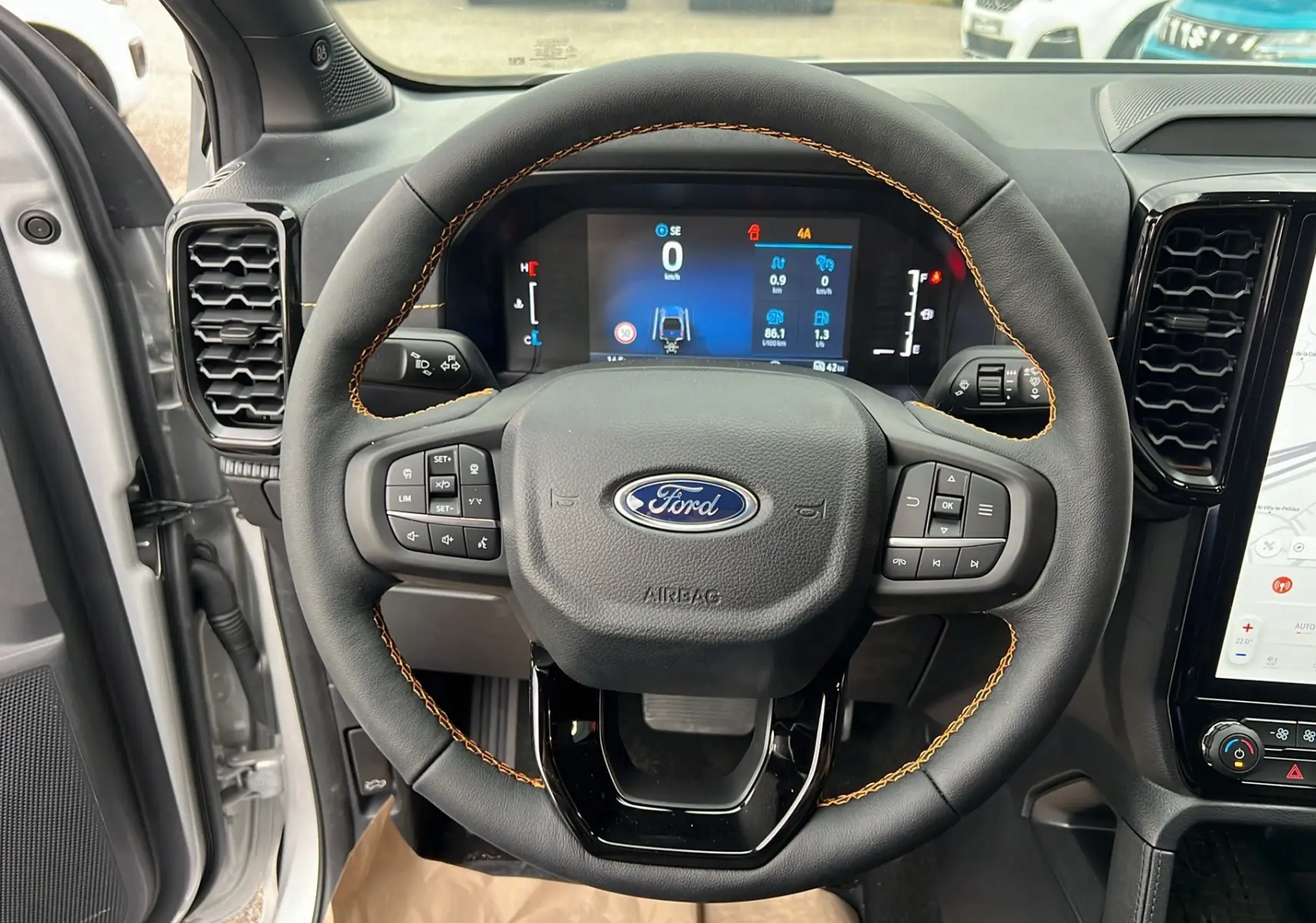 Vue intérieure centrée sur le volant cuir noir avec surpiqûres orange du Ford Ranger 2025 gris iconic.