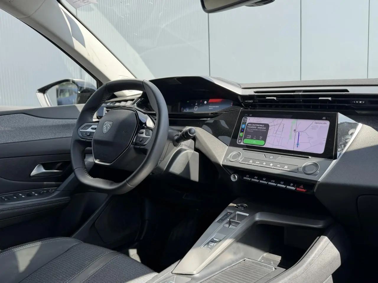 Vue intérieure côté conducteur du Peugeot 308 SW 2025 noir Perla, avec tableau de bord moderne et écran tactile central affichant la navigation.