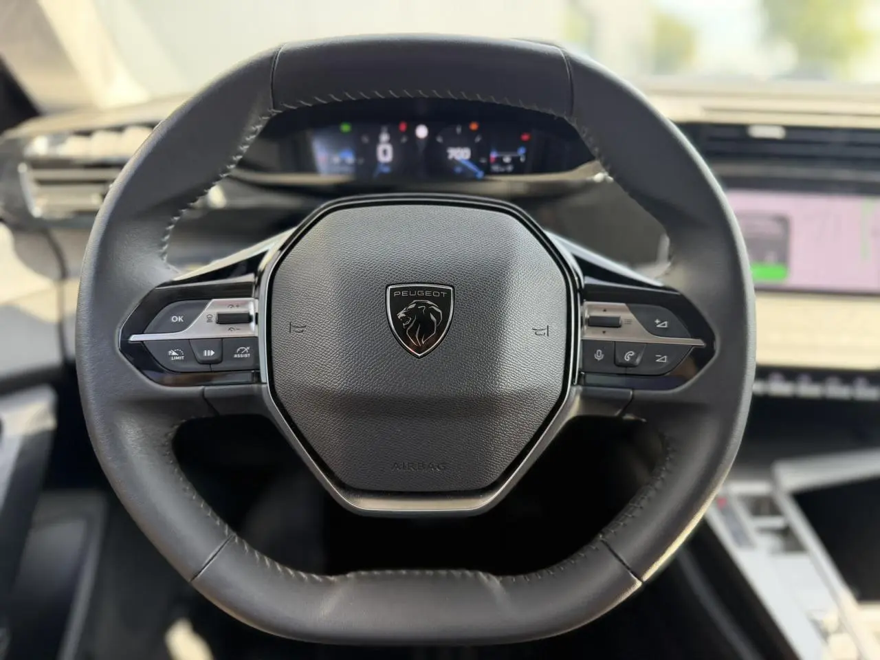 Vue rapprochée du volant cuir noir de la Peugeot 308 SW 2025 avec commandes intégrées et tableau de bord digital flou.