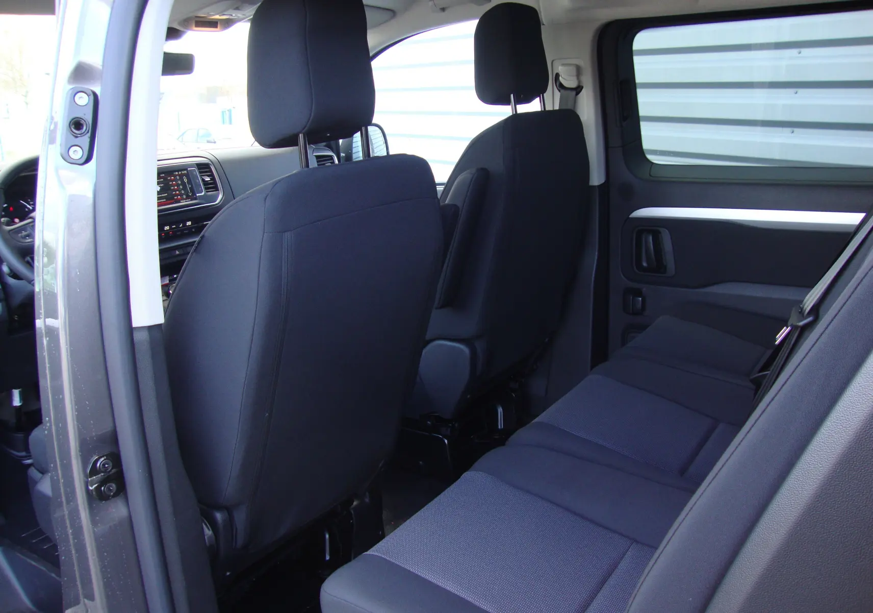Vue intérieure côté droit du Citroën Jumpy XL gris platinum, montrant les sièges arrière et avant en tissu noir.