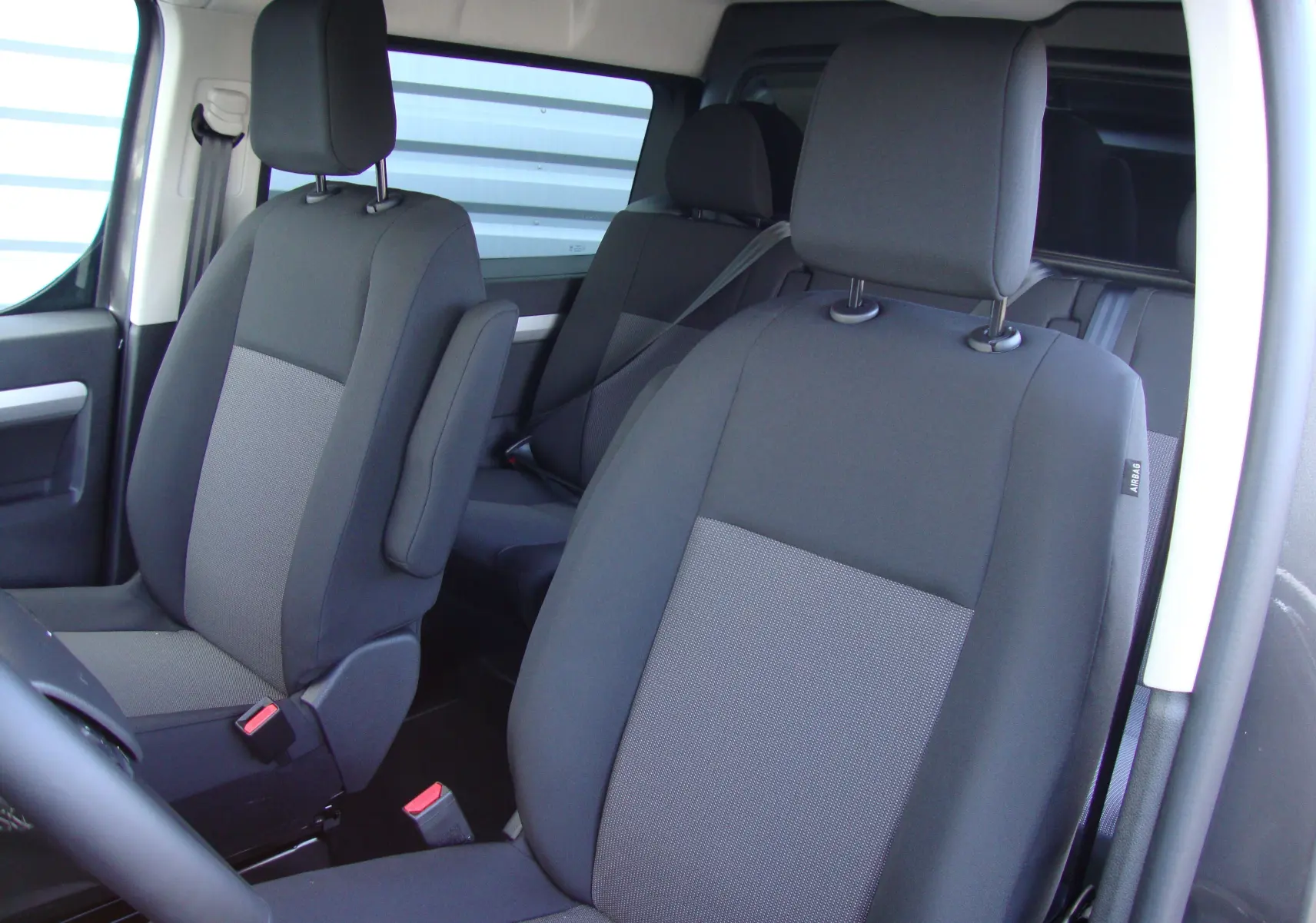 Vue intérieure des sièges avant et arrière en tissu gris foncé du Citroën Jumpy Cabine Approfondie XL 2024.