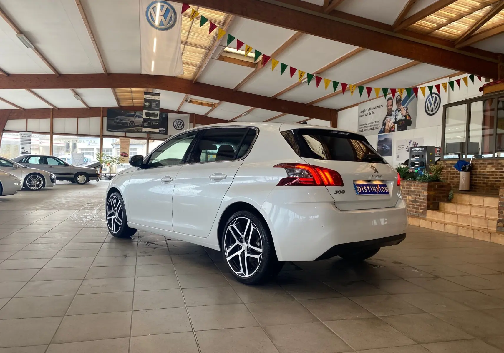 Peugeot 308 blanche vue 3/4 arrière droit dans un showroom avec jantes alliage et vitres teintées.