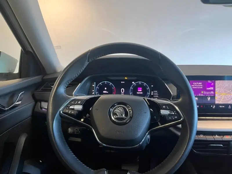 Vue centrée sur le volant cuir multifonction d'une Skoda Octavia Combi blanche, avec tableau de bord digital et écran tactile visible à droite.