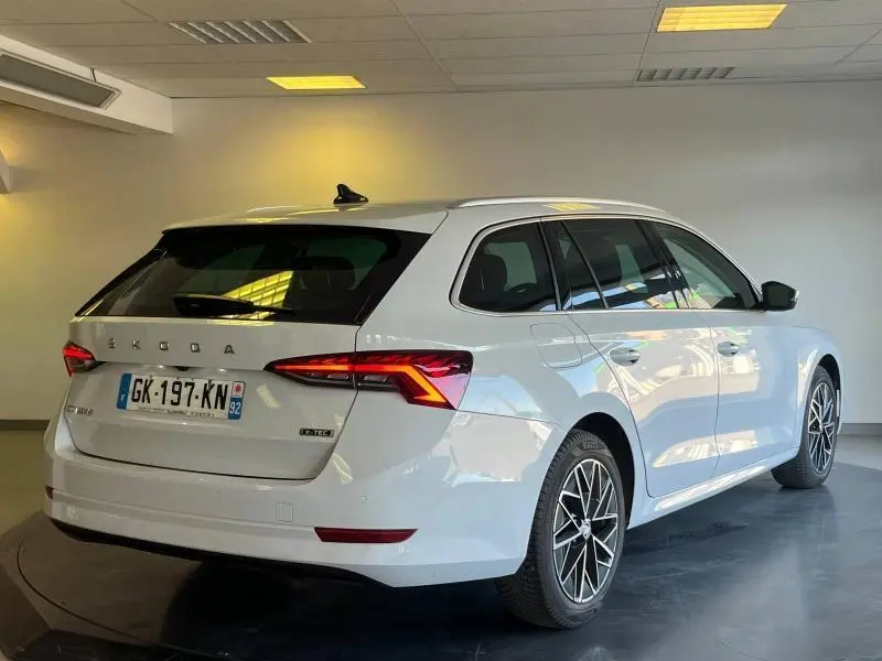 Vue 3/4 arrière droite d'une Skoda Octavia Combi blanche Cristal spéciale avec feux LED et jantes alu en intérieur showroom.