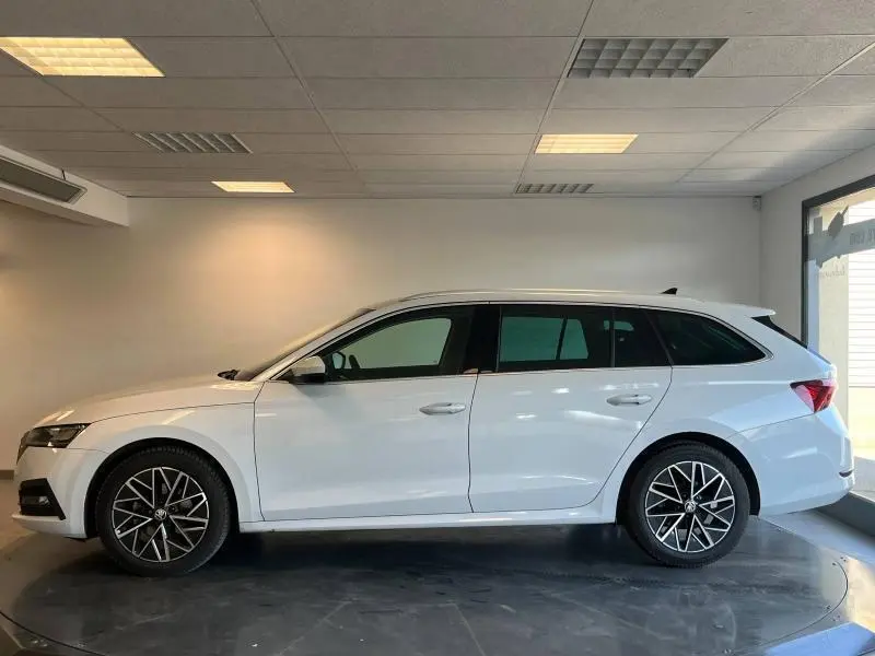Vue latérale droite d'une SKODA OCTAVIA COMBI blanche Cristal spéciale avec jantes alliage et vitres teintées dans un showroom.