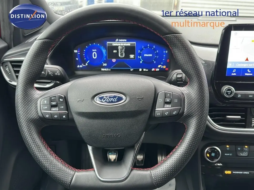 Vue rapprochée du volant perforé avec surpiqûres rouges et tableau de bord numérique de la Ford Puma rouge 2020.