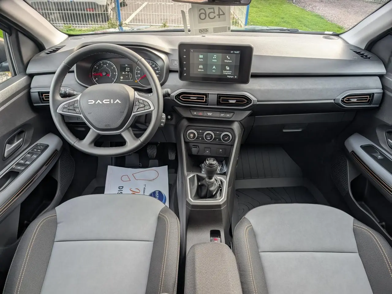 Vue intérieure avant du Dacia Jogger 2025, tableau de bord noir avec volant multifonction et sellerie mixte gris avec surpiqûres brunes.