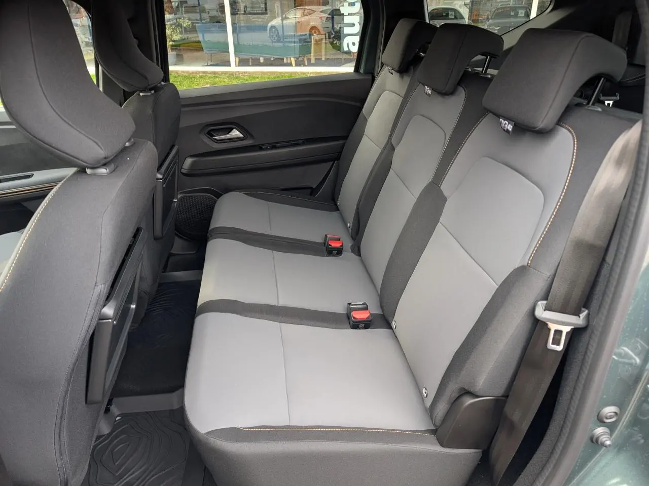 Vue latérale intérieure du siège arrière gris clair et noir du Dacia Jogger 2025, avec appuie-têtes et ceintures visibles.