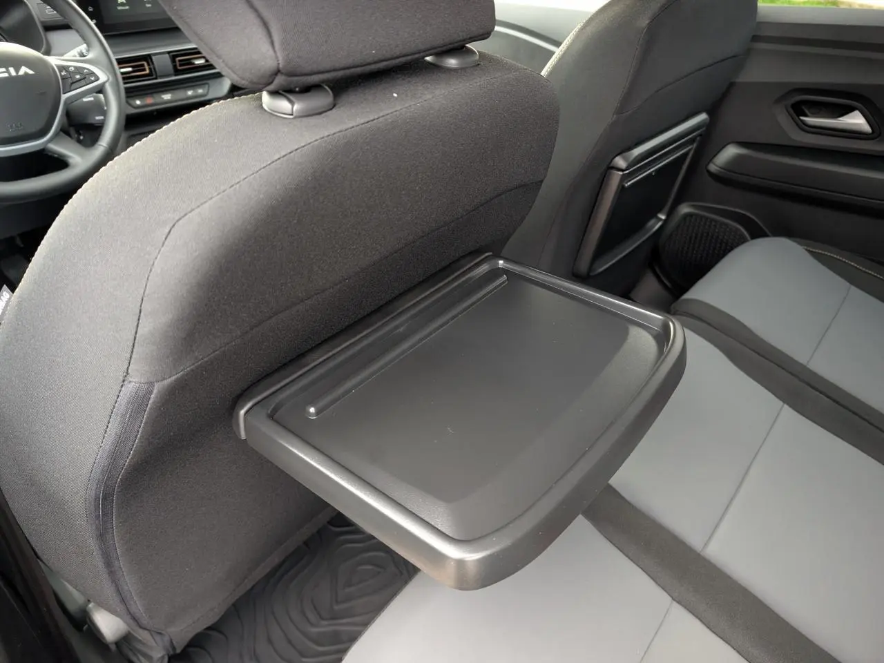 Vue intérieure arrière droite du Dacia Jogger 2025, avec tablette rabattable sur le dossier du siège avant et sellerie bicolore.