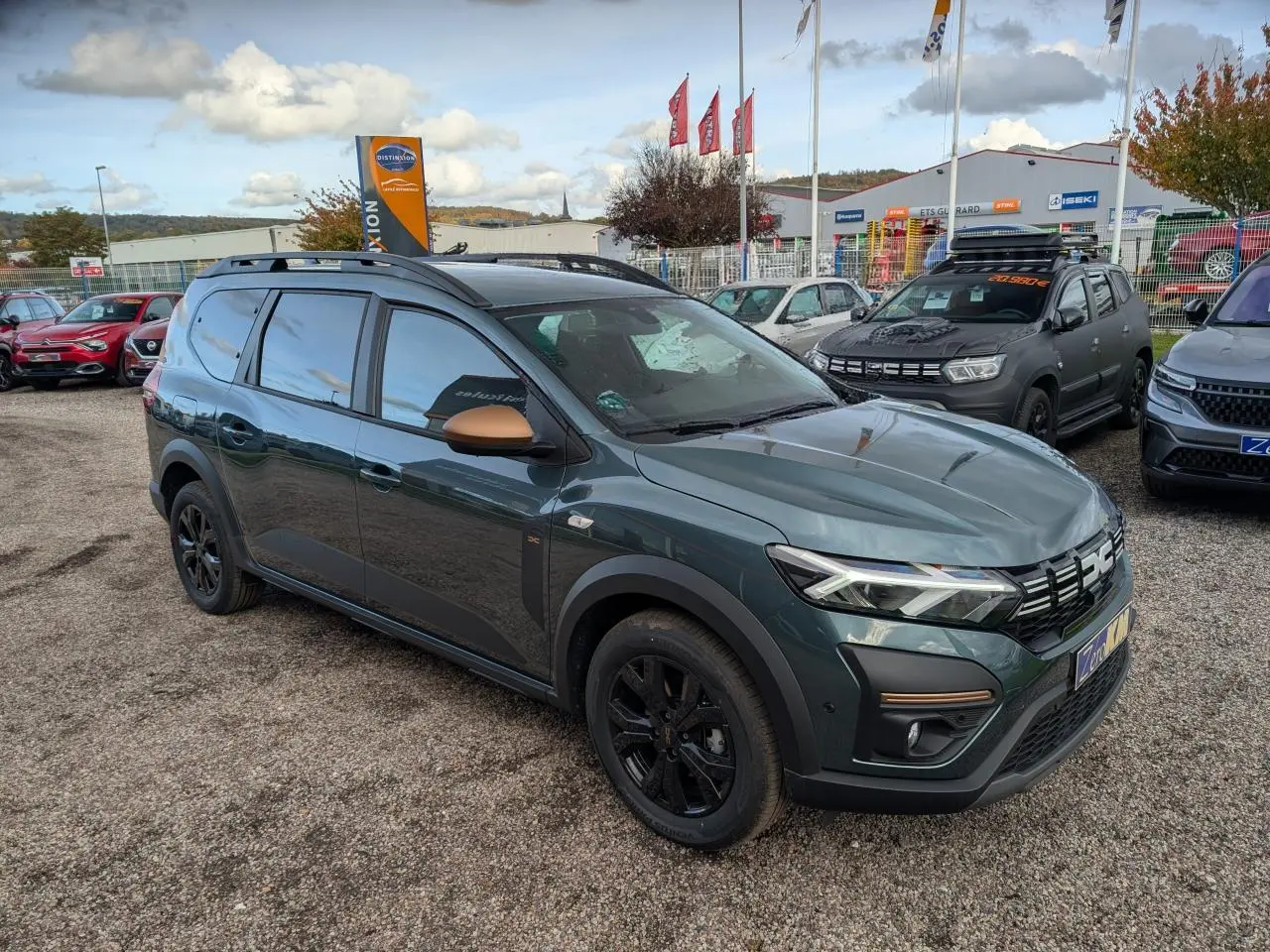 Dacia Jogger 2025 vert métallisé en 3/4 avant droit, avec rétroviseurs brun cuivré et jantes noires.