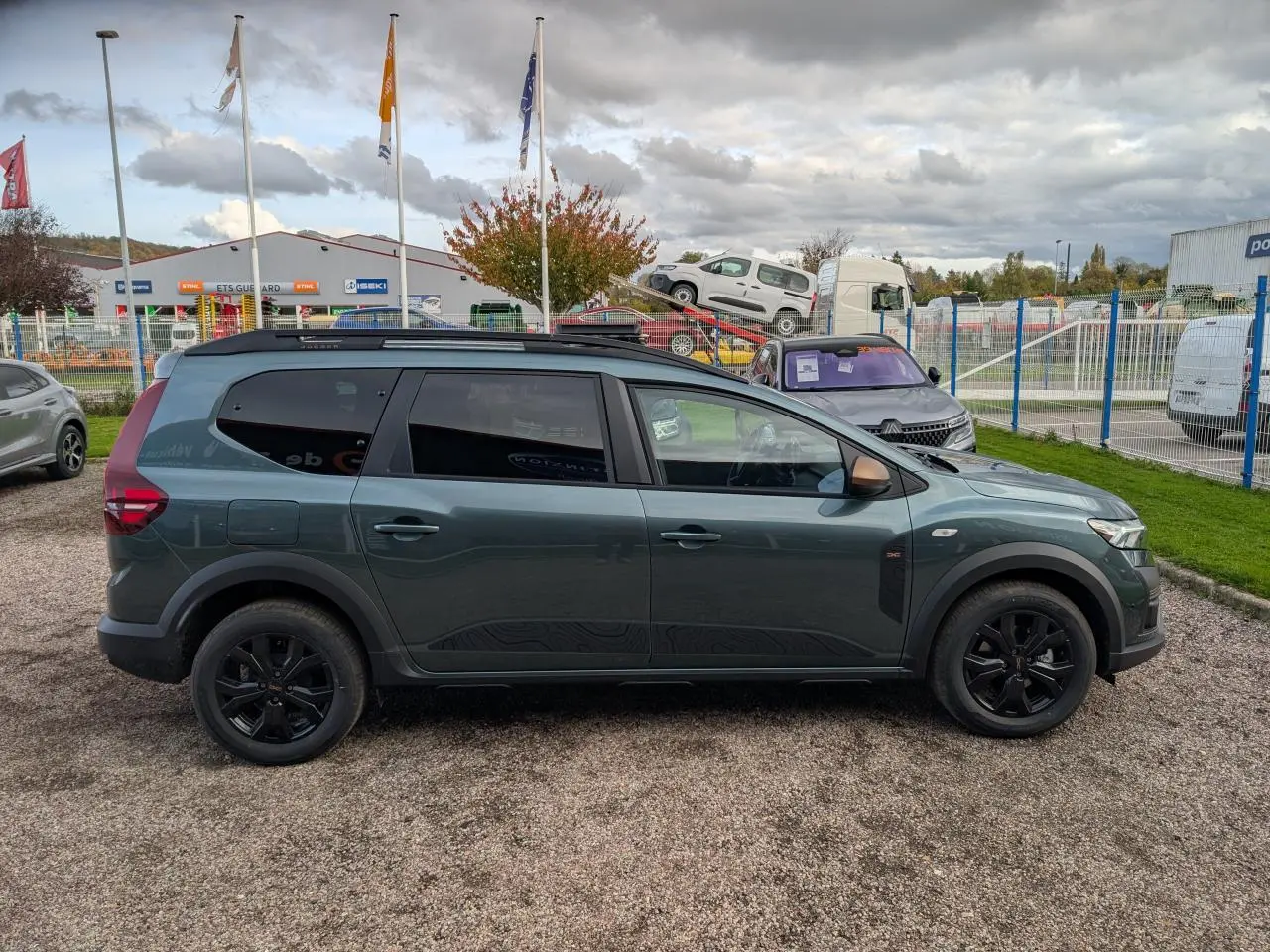 Vue de profil côté gauche d’un Dacia Jogger vert métallisé avec jantes noires et barres de toit noires.