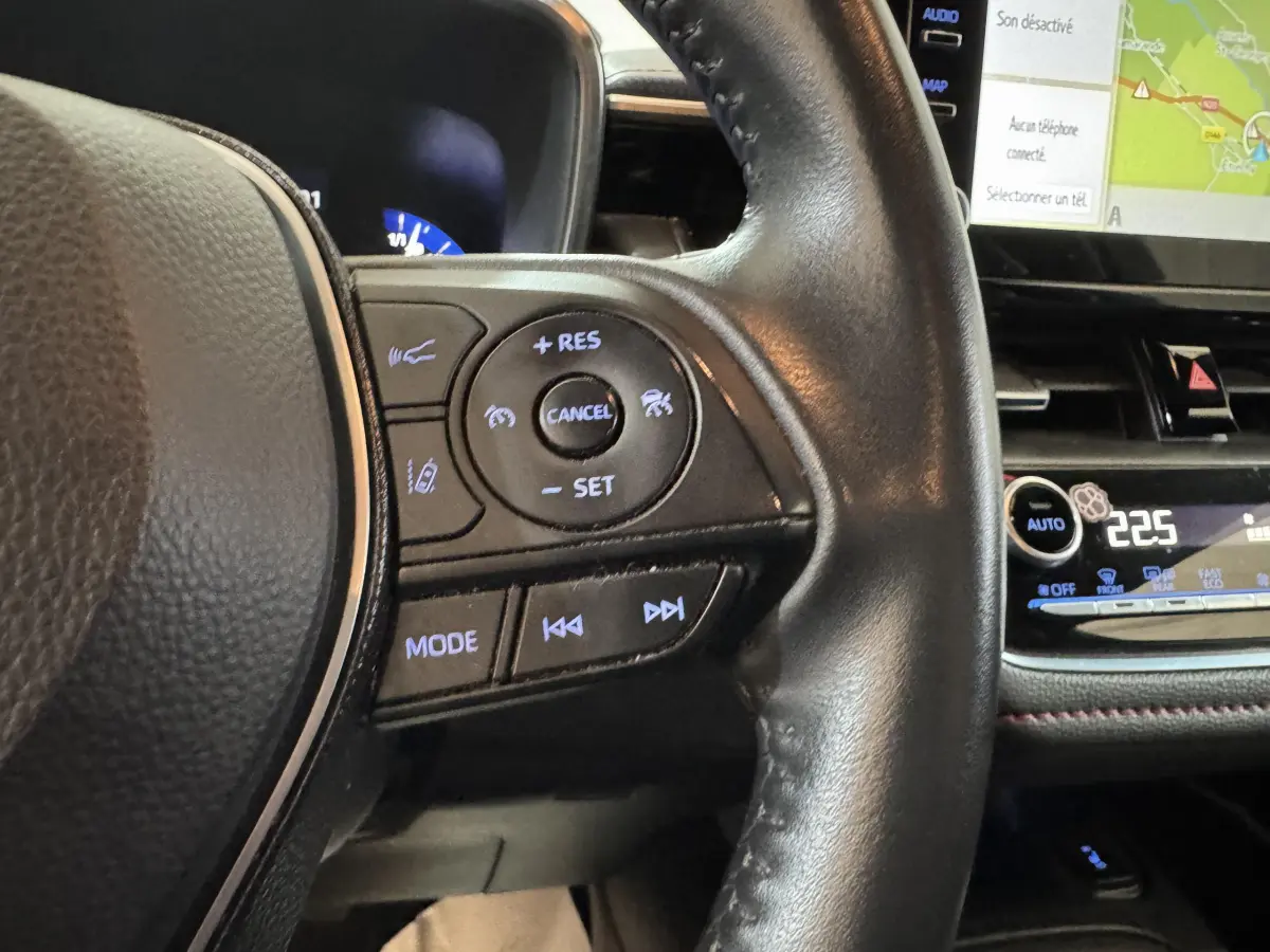 Gros plan sur le volant cuir noir de la Toyota Corolla Hybride 122h 2021 avec commandes multifonctions et écran tactile visible.