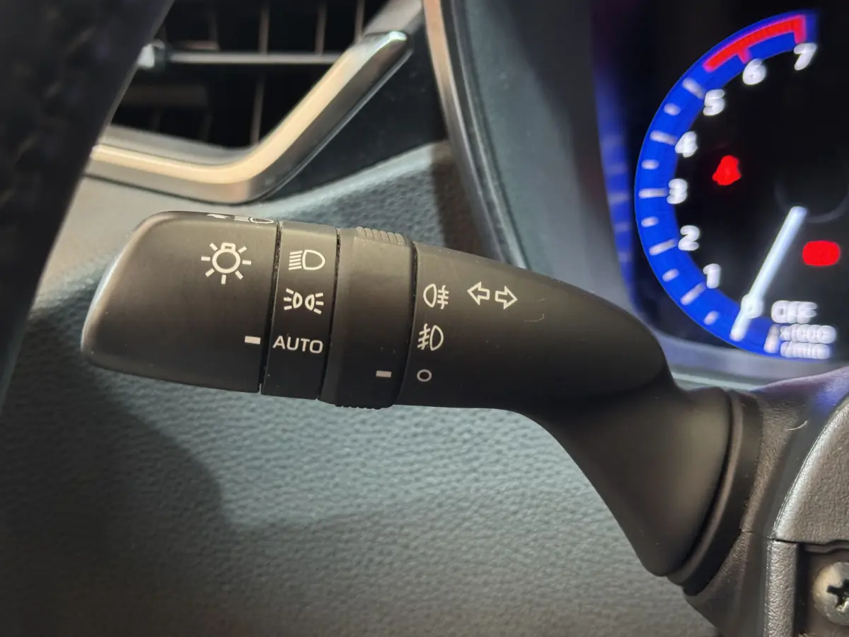 Gros plan sur la commande des phares avec réglages automatiques, dans l'habitacle gris d'une Toyota Corolla hybride 2021.