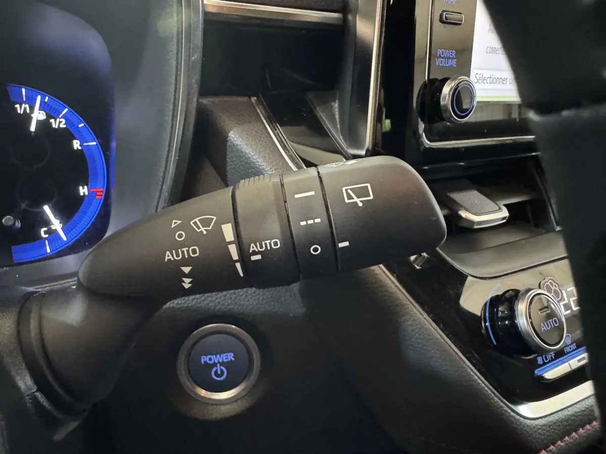 Gros plan sur la commande d’essuie-glace et le bouton Power bleu du tableau de bord d’une Toyota Corolla hybride gris clair.