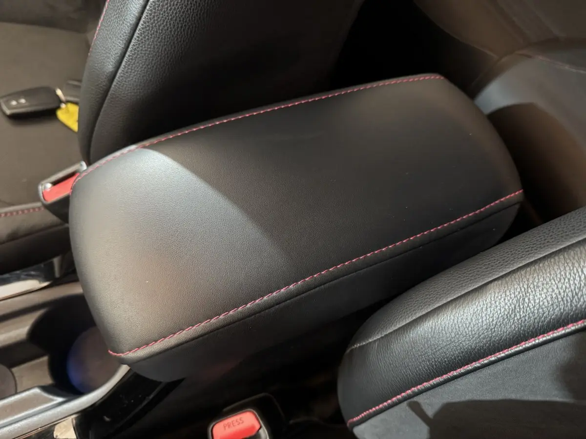 Accoudoir central en cuir noir avec surpiqûres rouges dans l'habitacle de la Toyota Corolla hybride 2021.