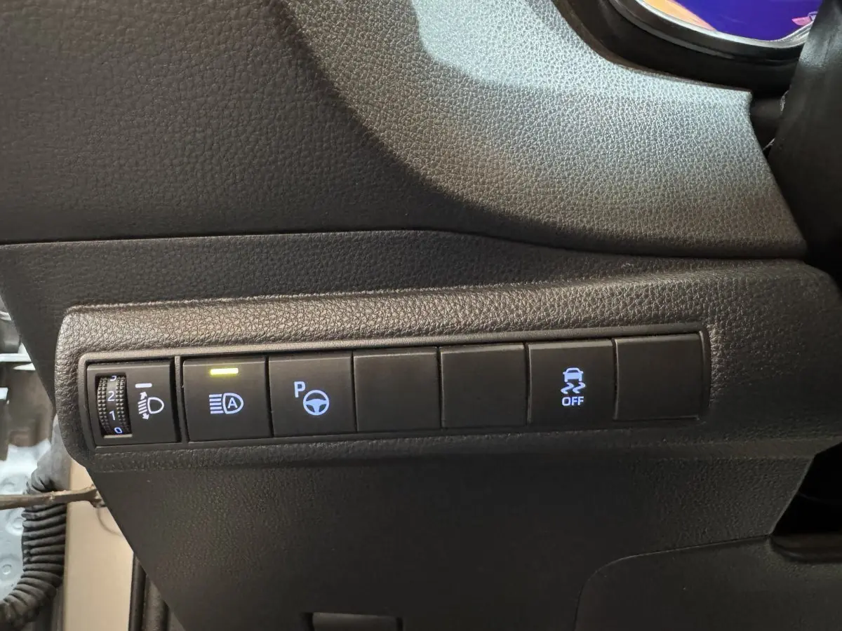 Panneau de commandes noires avec boutons d'assistance au stationnement et contrôle de phares dans une Toyota Corolla hybride gris clair 2021.