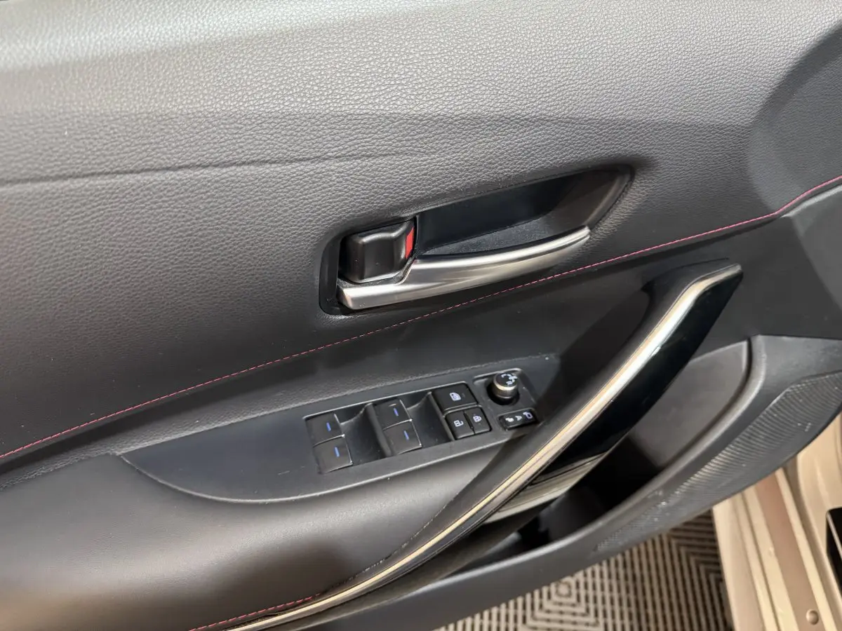 Gros plan sur la porte côté conducteur de la Toyota Corolla Hybride 122h Collection 2021 avec garniture noire et surpiqûres rouges.