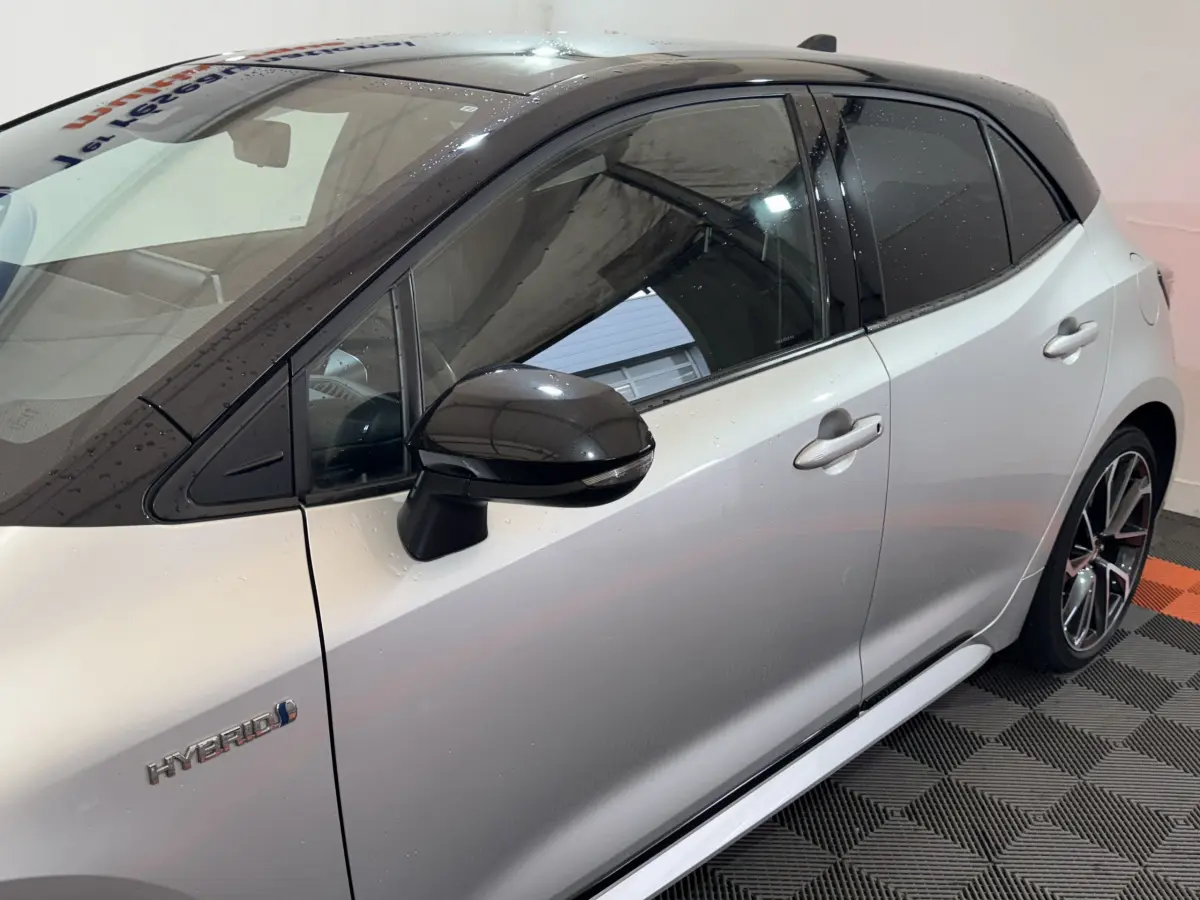 Vue de profil côté gauche d'une Toyota Corolla Hybride gris clair avec toit noir et rétroviseur noir brillant.