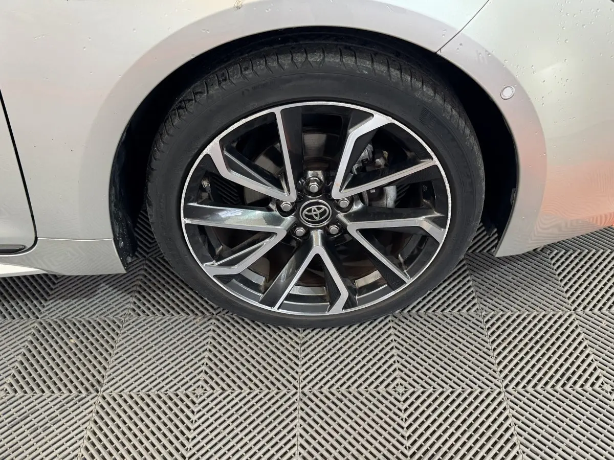 Gros plan sur la roue avant gauche de la Toyota Corolla Hybride 122h Collection gris clair avec jante alliage bicolore.