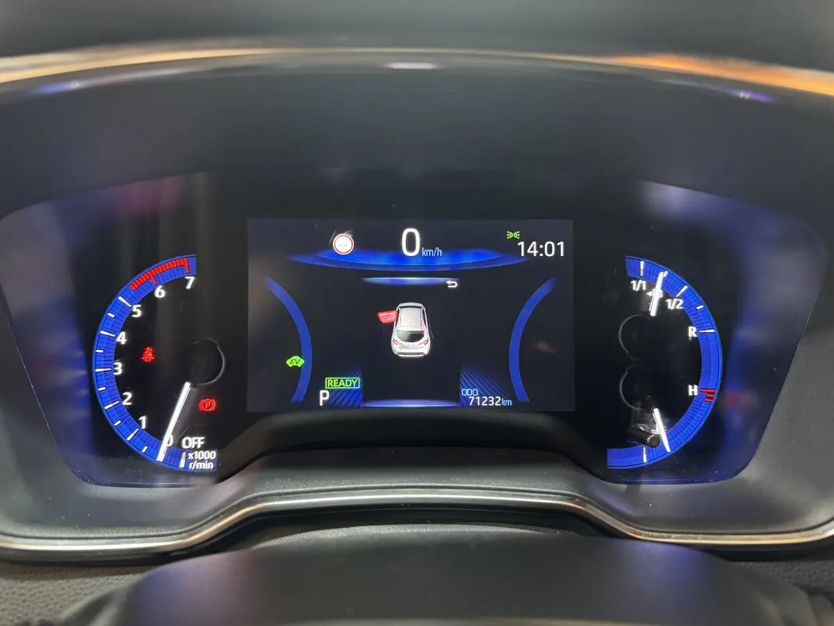 Tableau de bord numérique de Toyota Corolla Hybride 122h gris clair, affichage central avec compteurs bleus et informations de conduite.