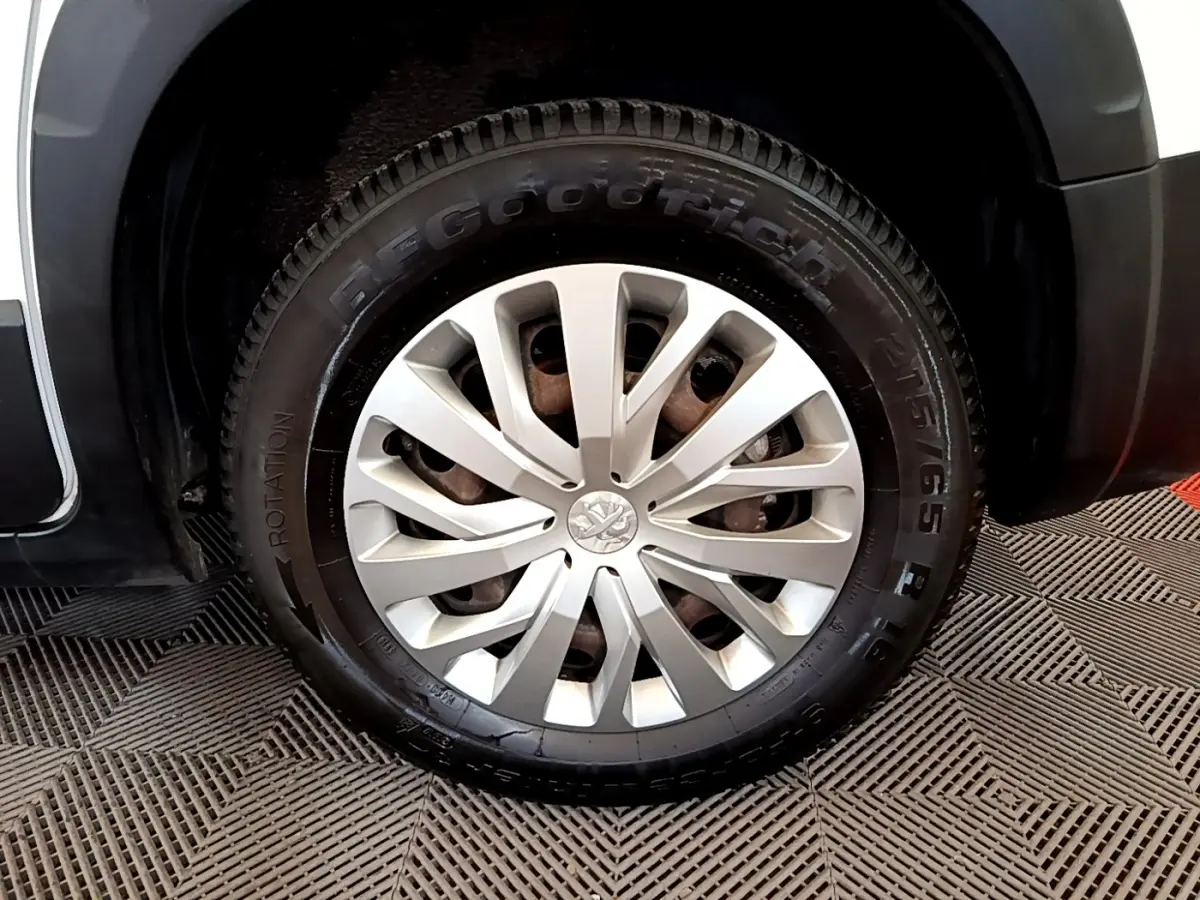 Gros plan sur la roue avant droite du Peugeot Rifter blanc, avec jante alliage et logo Peugeot central.